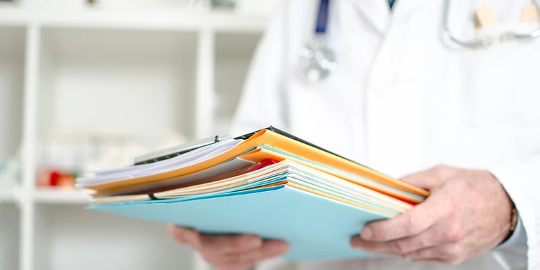 Arzt hält mehrere Patientenakten in verschiedenen Farben in den Händen.