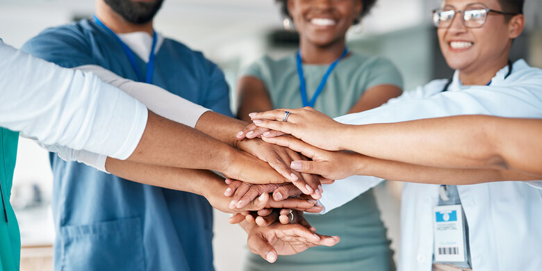 Medizinisches Team legt Hände übereinander als Zeichen des Zusammenhalts. Teamarbeit im Gesundheitswesen.