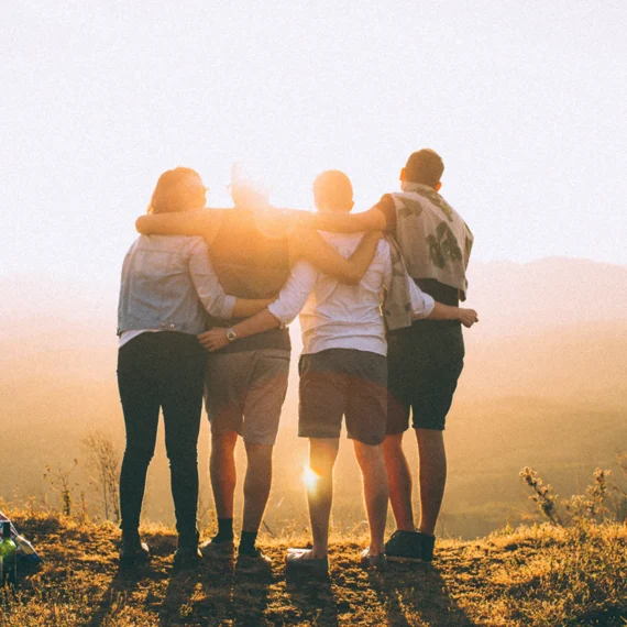 Vier Personen stehen im Sonnenuntergang auf einem Hügel eng beieinander und genießen den Ausblick in die Landschaft.