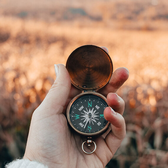 Eine Hand hält einen geöffneten Kompass in herbstlicher Natur, bereit, den richtigen Weg zu finden.