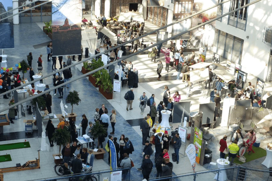 Informationsmesse zum Tag des Gesundheitsamtes: Vogelperspektive auf Ausstellungsfläche mit Infoständen, Besuchern und Sitzgelegenheiten.