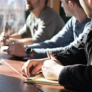 Teilnehmer bei Workshop oder Planungstreffen. Eine Person macht Notizen. Symbolisiert Zusammenarbeit, Ideenentwicklung und Beteiligungsprozesse.