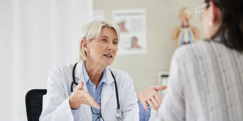 Ärztin mit Stethoskop im Gespräch mit Patientin in heller Praxis.