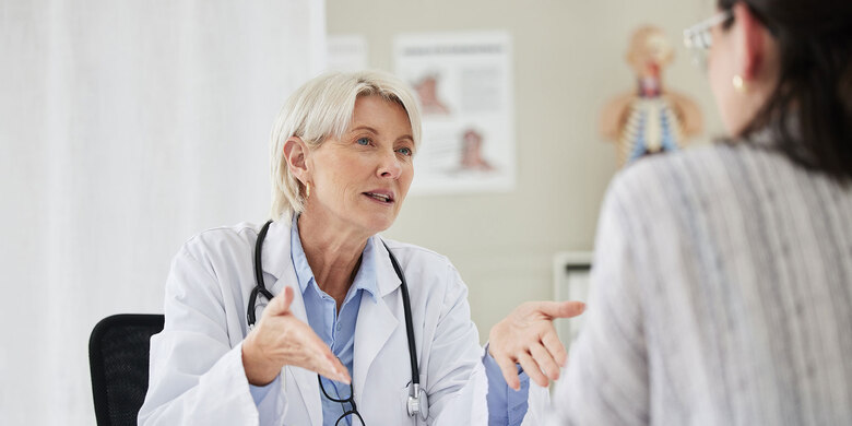 Ärztin mit Stethoskop im Gespräch mit Patientin in heller Praxis.