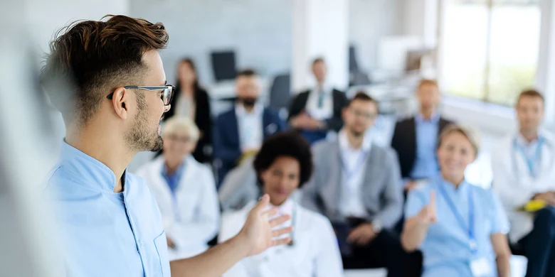 Mann mit Brille hält Vortrag vor Gruppe von Zuhörenden in hellem Schulungsraum im Rahmen einer Fortbildung.