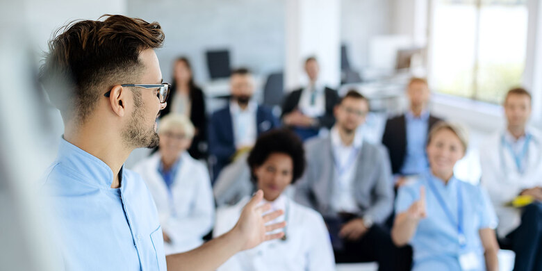 Mann mit Brille hält Vortrag vor Gruppe von Zuhörenden in hellem Schulungsraum im Rahmen einer Fortbildung.