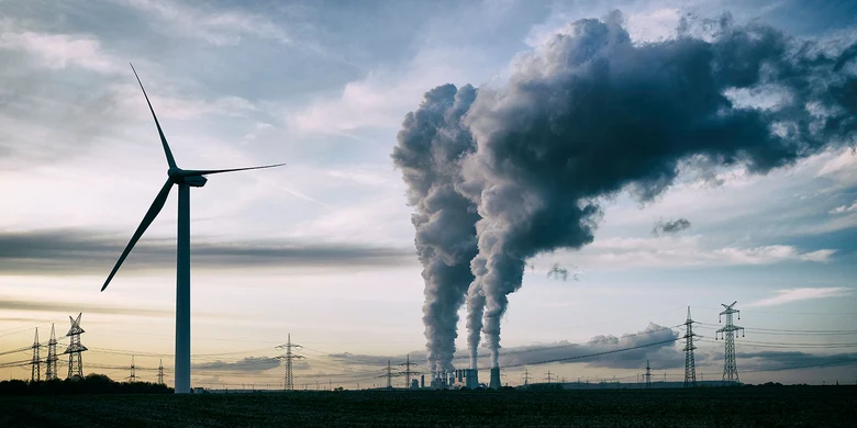 Windrad links, Kraftwerk mit Dampfwolken mittig, Strommasten im Hintergrund, Dämmerungshimmel.