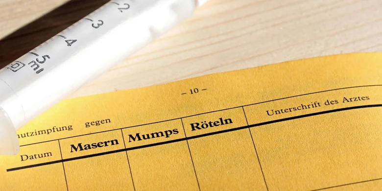 Gelber Impfausweis mit Tabelle für Masern-, Mumps-, Rötelnimpfungen, Datum und Arztunterschrift, Impfspritze oben links.