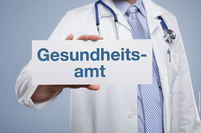 Arzt mit Kittel hält ein Schild in die Kamera auf dem steht Gesundheitsamt.
