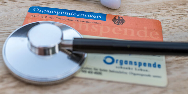 Organspendeausweis und Organspendeerklärung mit Stethoskop auf Holztisch.