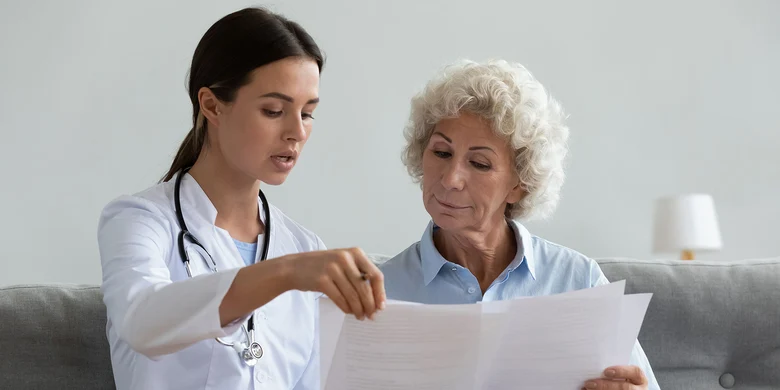 Ärztin erklärt älterer Patientin Dokument. Beratungsgespräch im medizinischen Kontext.