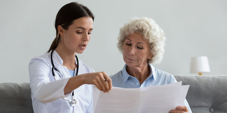 Ärztin erklärt älterer Patientin Dokument. Beratungsgespräch im medizinischen Kontext.