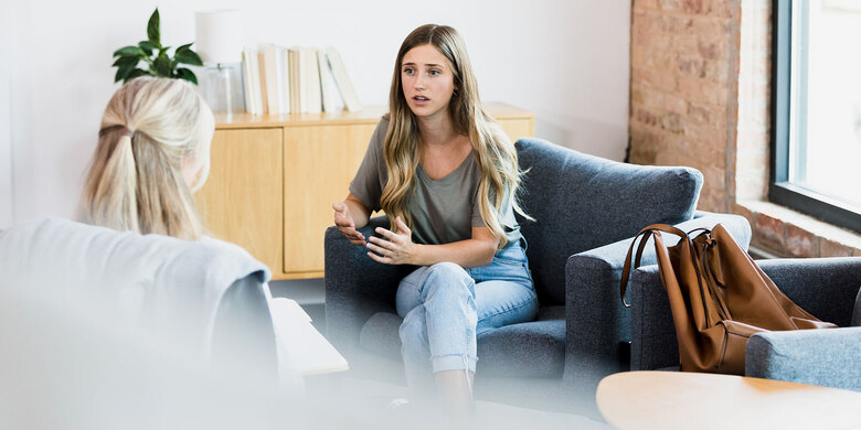 Junge Frau im Beratungsgespräch auf grauem Sofa. Therapeutische Gesprächssituation.