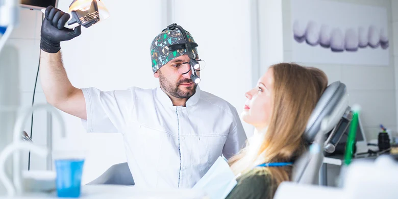 Foto von einer Zahnarztpraxis. Patientin liegt auf der Liege, der Zahnarzt sitzt daneben, bereit zur Behandlung.