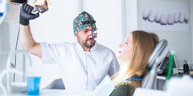 Foto von einer Zahnarztpraxis. Patientin liegt auf der Liege, der Zahnarzt sitzt daneben, bereit zur Behandlung.