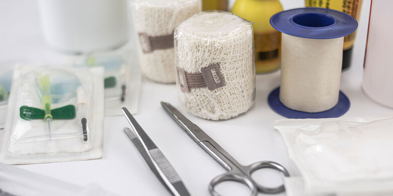 Verbandmaterial, Schere, Pinzette und medizinische Utensilien auf weißer Unterlage. Erste-Hilfe-Ausstattung.