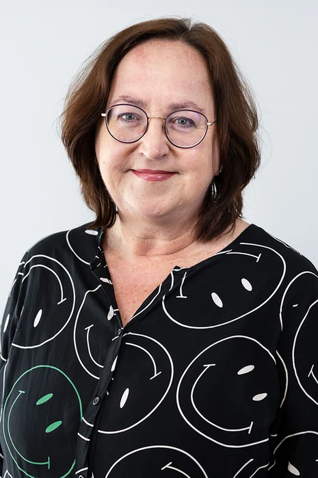 Dr. med. Uta Katharina Schmidt-Göhrich, Porträt einer Frau mit Brille und braunem Haar in schwarzer Bluse mit Smiley-Muster vor hellem Hintergrund.