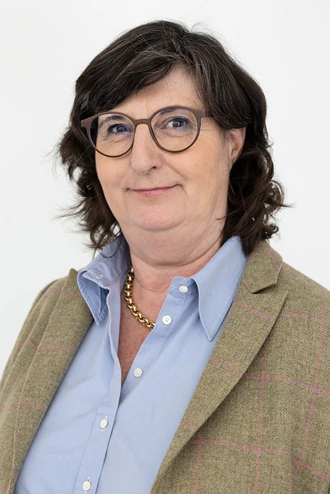 Dr. med. Sophie Susann Merbecks, Porträt einer Frau mit Brille und dunklem Haar in grauem Blazer mit Karomuster über hellblauer Bluse und goldener Kette vor hellem Hintergrund.