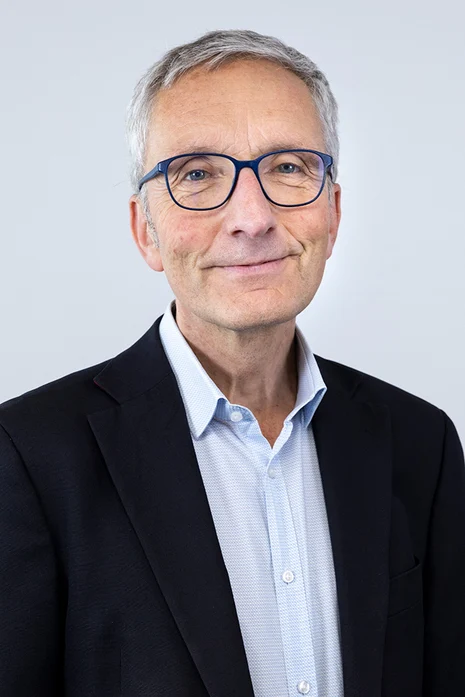 Prof. Dr. Reinhard Berner, Porträt eines älteren Mannes mit Brille in schwarzem Sakko über hellblauem Hemd vor hellem Hintergrund.