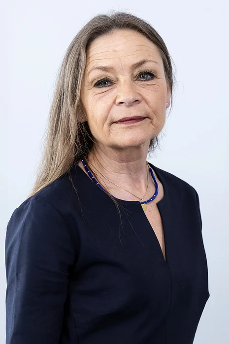 Susanne Liebe, Porträt einer Frau mit langem Haar in schwarzer Bluse mit blauer Kette vor hellem Hintergrund.