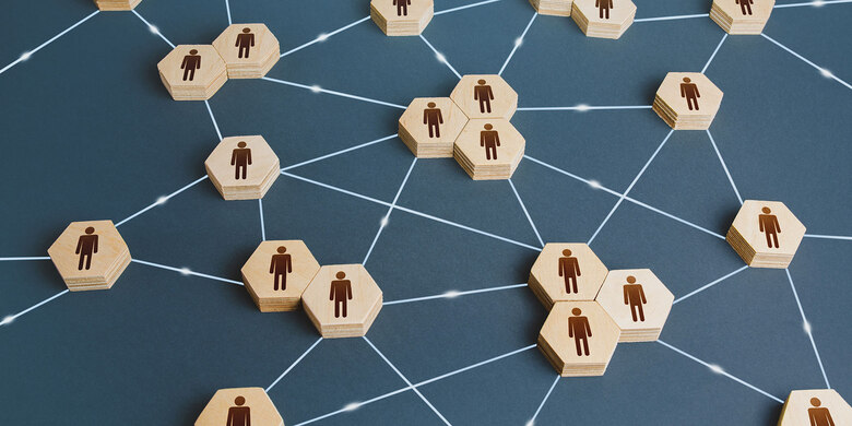 Symbolische Darstellung von Organisationsstrukturen: Sechseckige Holzplättchen mit Personensymbolen sind durch leuchtende Netzwerklinien verbunden.