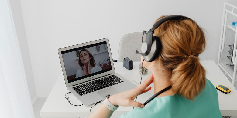 Telemedizinische Beratung: Person mit Kopfhörern nimmt an einer Videosprechstunde am Laptop teil und kommuniziert mit medizinischem Fachpersonal.