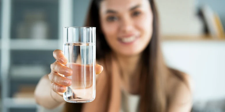 Frau hält Glas mit Trinkwasser in die Kamera, symbolisiert die Überwachung der Trinkwasserqualität durch Gesundheitsämter.