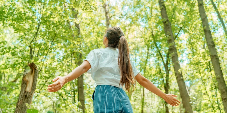 Mädchen mit ausgebreiteten Armen im Wald, symbolisiert positive Wirkung der Natur auf Gesundheit und Wohlbefinden im Rahmen des Umweltschutzes.