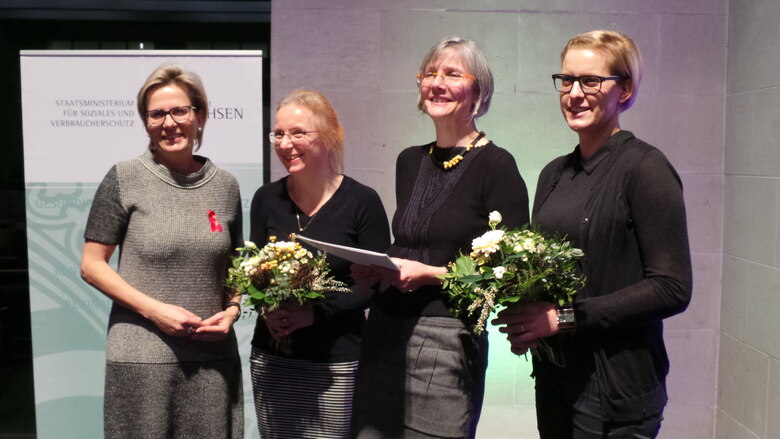 Verleihung der Sächsischen Ehrenmedaille für herausragende Leistungen im Kampf gegen HIV und AIDS 2015: Vier Preisträgerinnen mit Blumensträußen vor Ministeriumbanner.