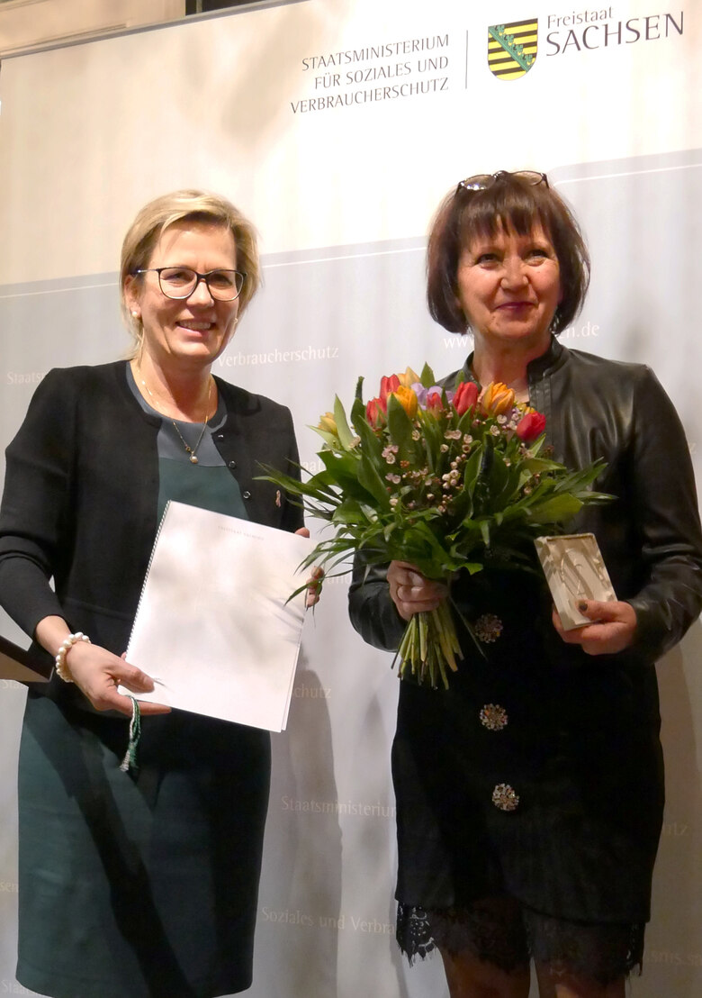 Verleihung der Sächsischen Ehrenmedaille für herausragende Leistungen im Kampf gegen HIV und AIDS 2018: Ministerin übergibt Tulpenstrauß und Medaille an Preisträgerin.